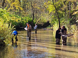 Community members stand in a creek and learn about aquatic habitats during a NICHES Program